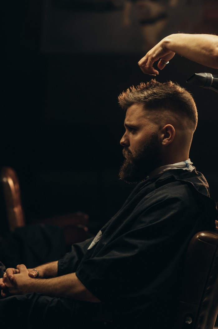 Junger bärtiger Mann lässt sich vom Friseur die Haare schneiden
